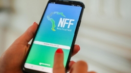 Mão segura um celular. Na tela, está o aplicativo Nota Fiscal Fácil, cuja tela tem as cores azul e verde.