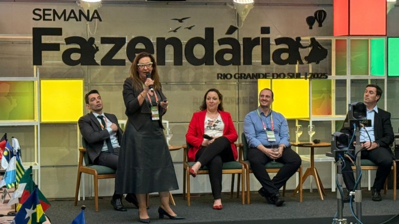 Jocie Pereira, Adriana Oliveira, Juliana Debaquer, Andr&eacute; Facchini e Edison Moro aparecem na imagem. Adriana est&aacute; em p&eacute;, com microfone, e os demais est&atilde;o sentados. Ao fundo, a inscri&ccedil;&atilde;o Semana Fazend&aacute;ria Rio Grande do Sul 2025.